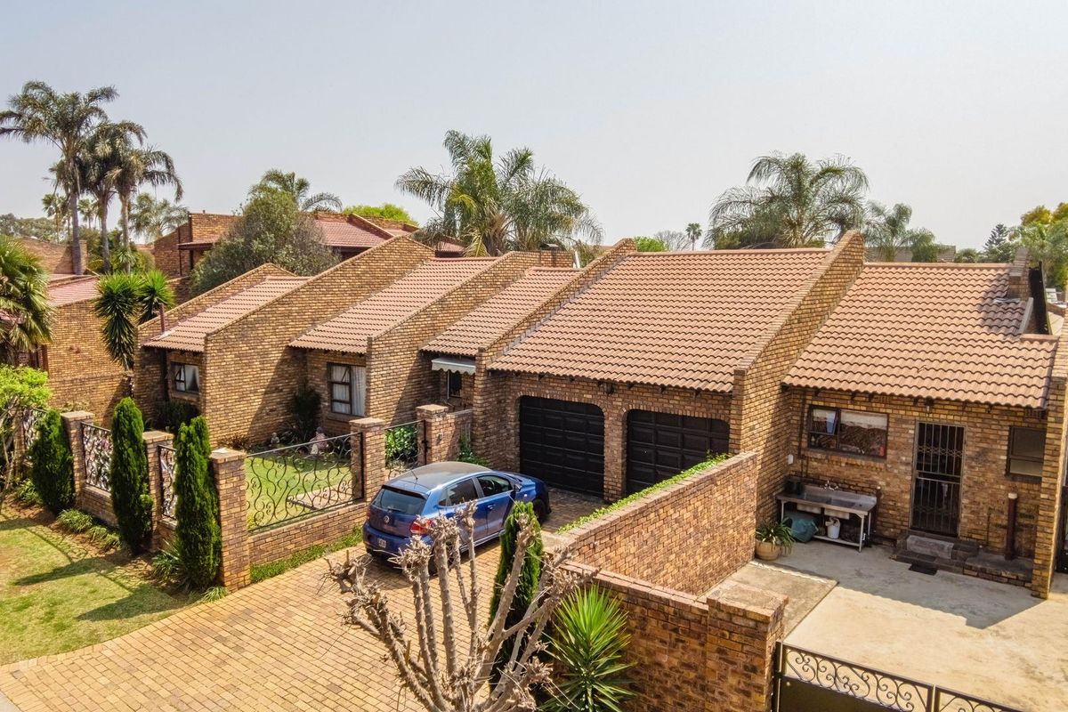 Aerial view of a face-brick residential property featuring a double garage, paved driveway, and established garden area.