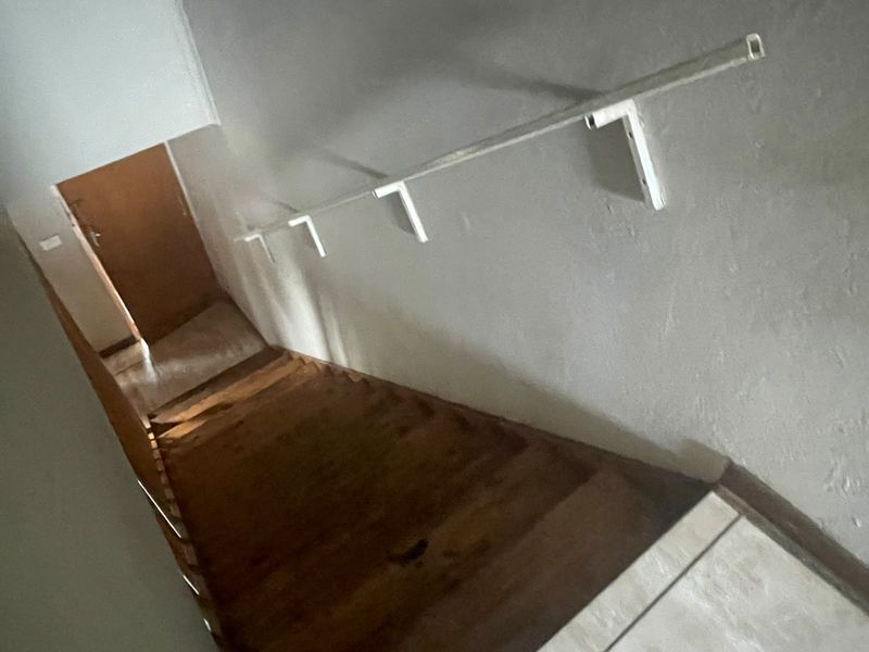 A view looking down a staircase featuring a simple wall-mounted handrail and wooden steps leading to a lower level.