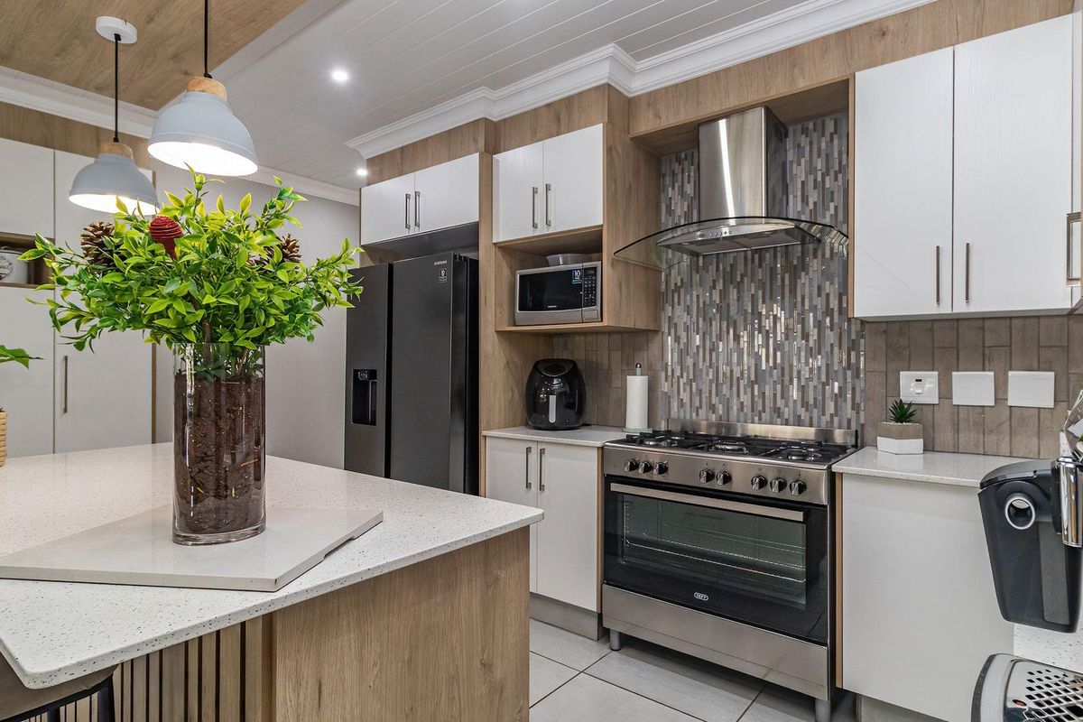 Modern kitchen featuring a central island with quartz countertops, gas stove, extractor fan, built-in microwave, and contemporary cabinetry with a tiled backsplash.