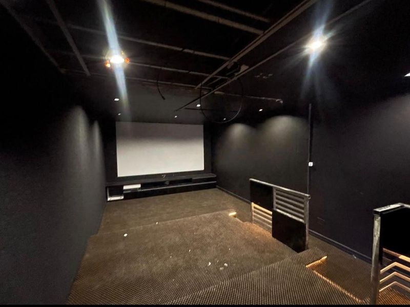 Dedicated cinema room featuring tiered flooring, a built-in media console, and a projector screen, currently requiring ceiling completion and finishing touches.