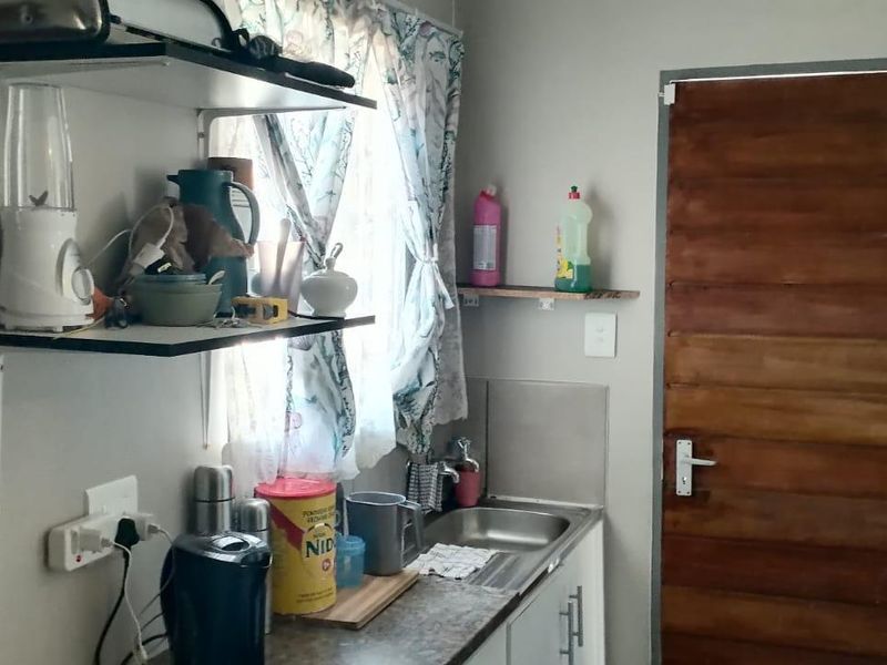 A compact kitchen area featuring a stainless steel sink, laminate countertop, base cabinetry, and wall-mounted shelving with a timber door.