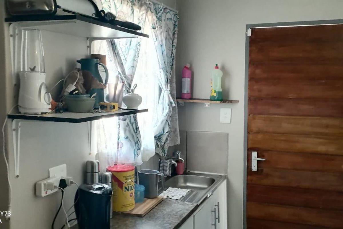 A compact kitchen area featuring a stainless steel sink, laminate countertop, base cabinetry, and wall-mounted shelving with a timber door.