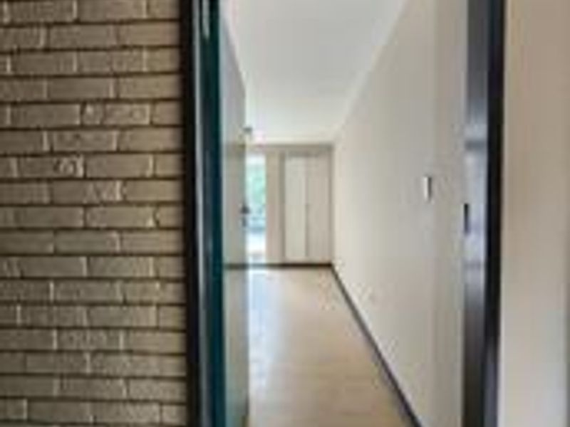 A view through a doorway into a long, empty hallway featuring tiled flooring and an exposed brick feature wall.