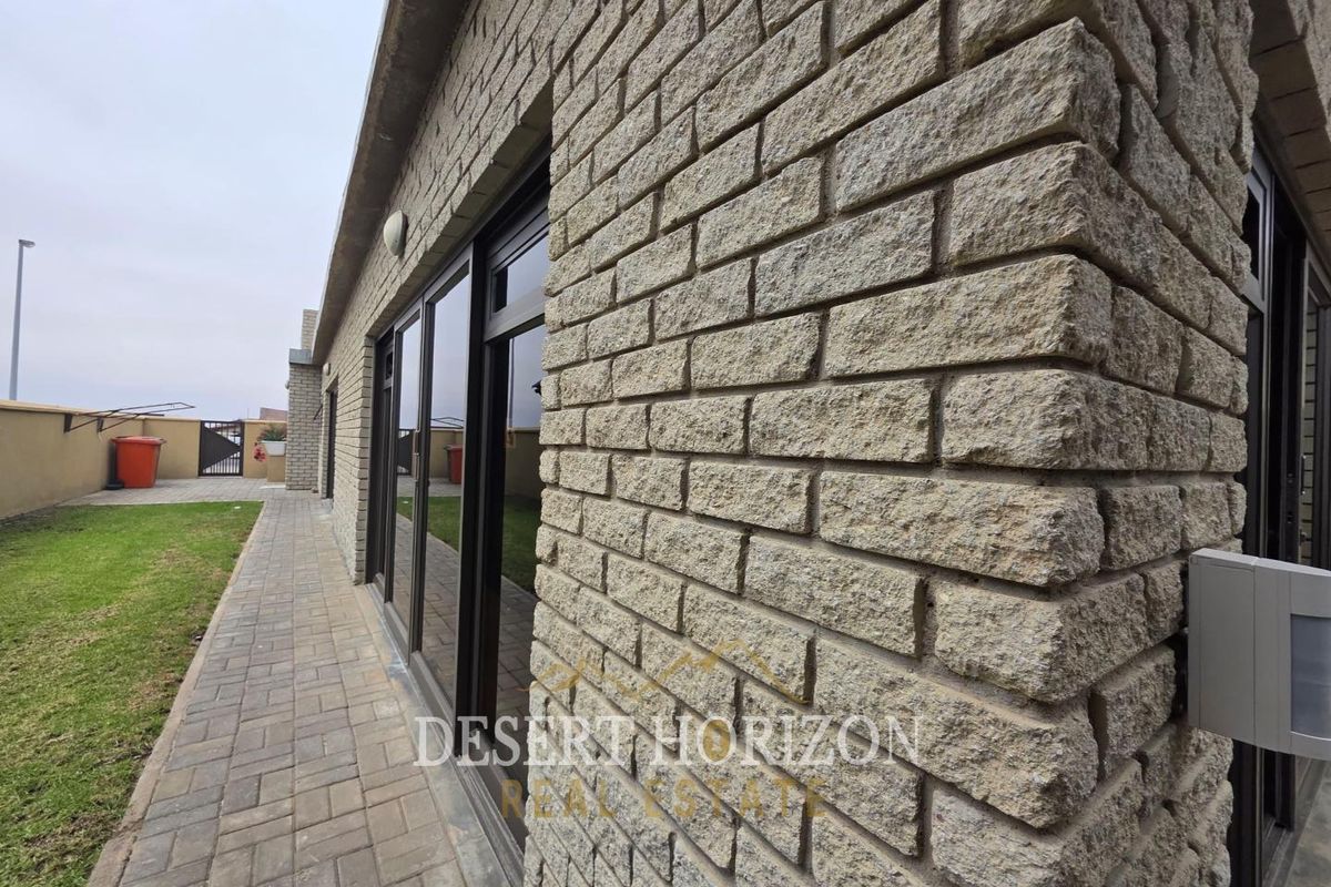 Rear exterior view featuring stone-clad walls, paved walkway, and large sliding glass doors leading to the garden area.