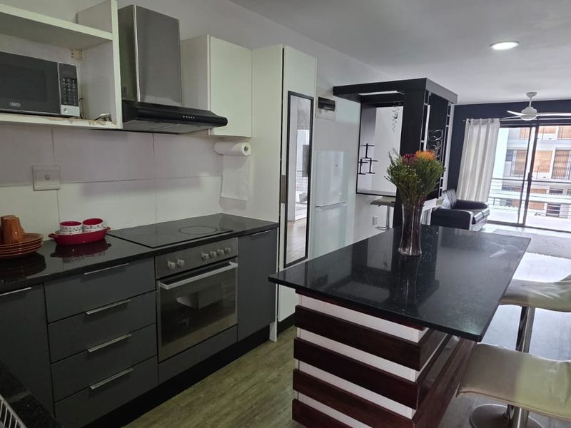 Modern open-plan kitchen and living area featuring a central island, built-in appliances, and direct access to a balcony through sliding doors.