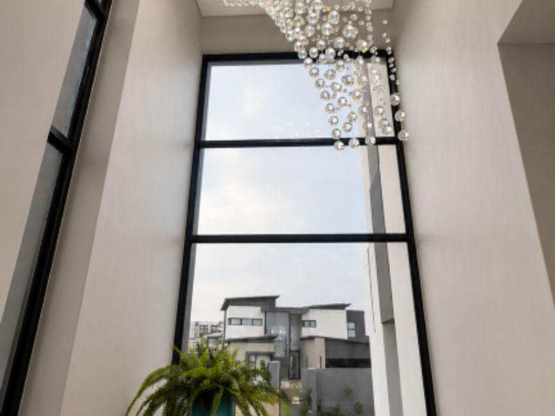 A bright and modern entrance hall featuring a striking crystal chandelier and expansive floor-to-ceiling windows that provide a clear view of the exterior.