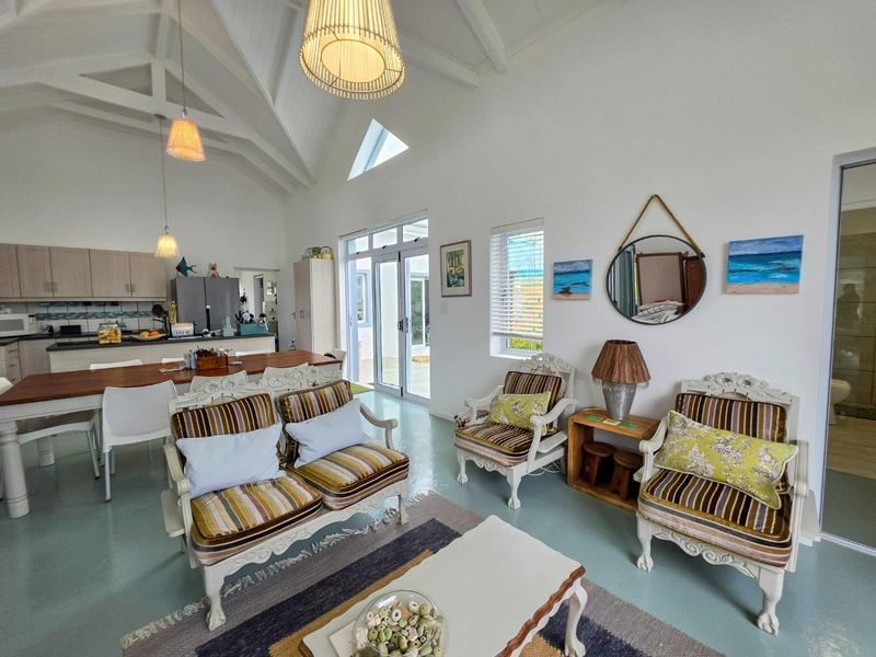 Bright open-plan living and kitchen area featuring vaulted ceilings with exposed rafters, modern epoxy flooring, and large glass sliding doors leading to the exterior.