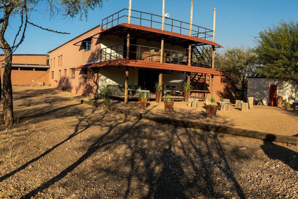 A multi-level small holding residence featuring a covered patio, upper-level balcony with metal railings, and a spacious gravel outdoor entertainment area.