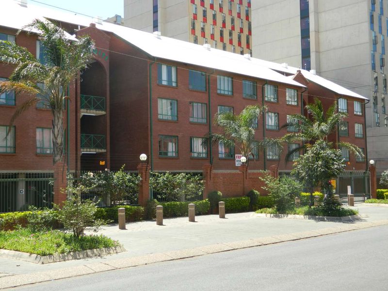 Front elevation of a multi-story brick apartment building featuring metal roofing, secure perimeter fencing, and gated access.