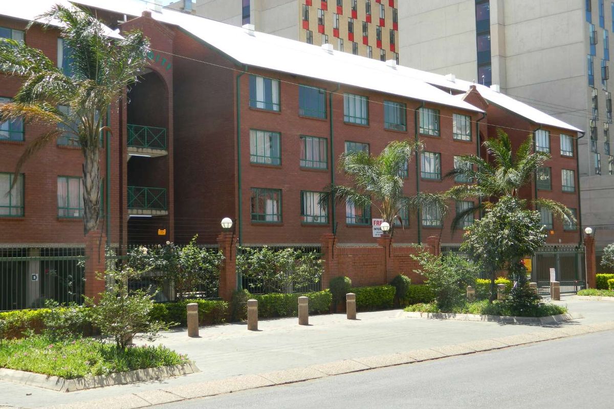 Front elevation of a multi-story brick apartment building featuring metal roofing, secure perimeter fencing, and gated access.