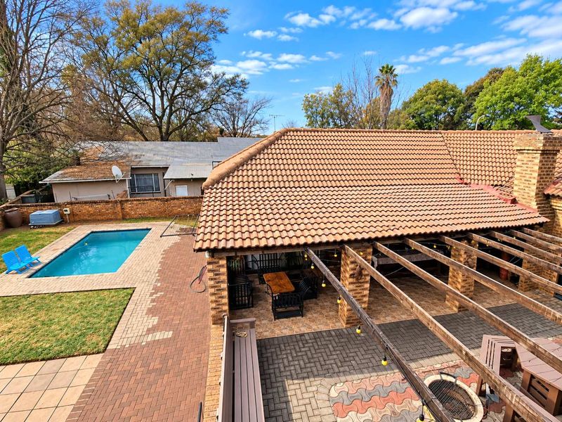Rear exterior view featuring a swimming pool, a covered patio area with a pergola, and a paved garden space with a built-in fire pit.