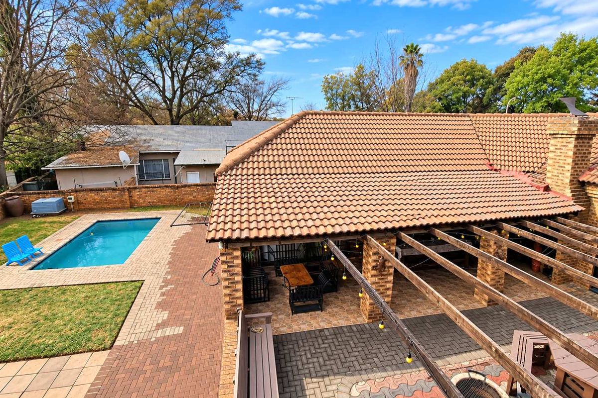 Rear exterior view featuring a swimming pool, a covered patio area with a pergola, and a paved garden space with a built-in fire pit.