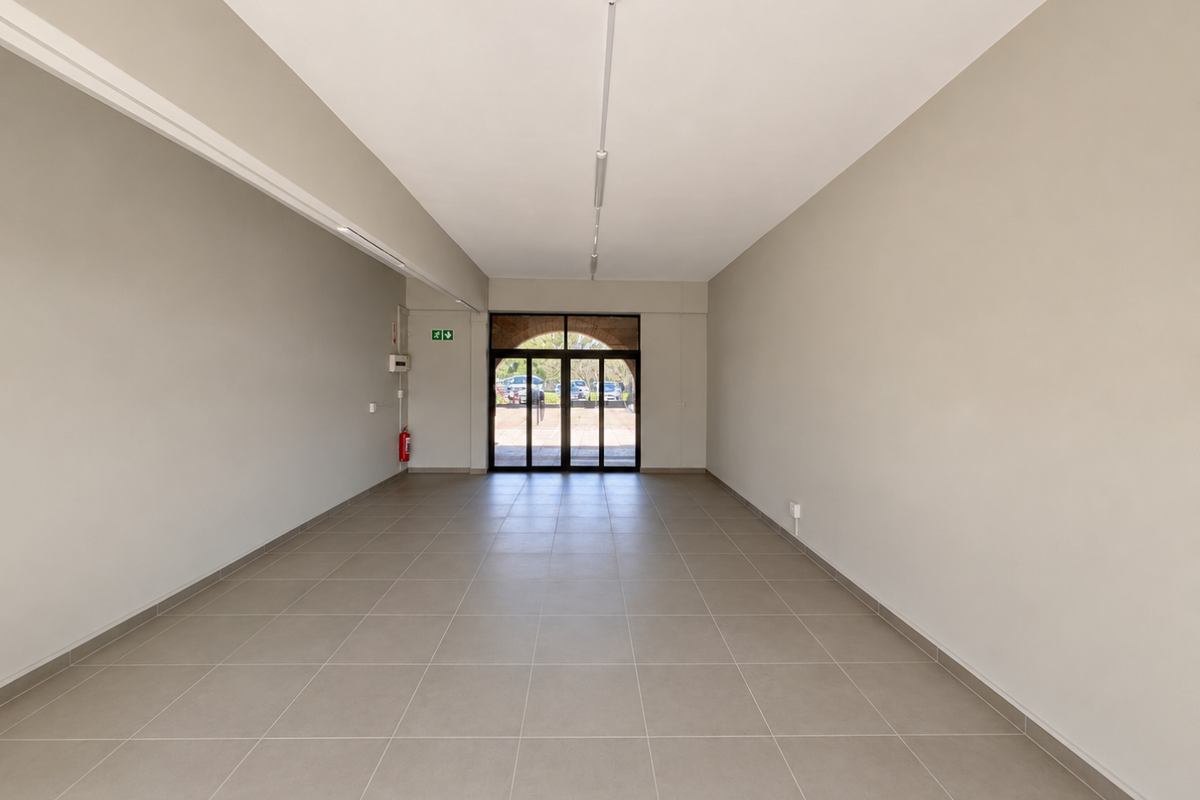 A spacious, empty open-plan retail unit featuring neutral tiled flooring, clean walls, and a large glass entrance door providing natural light.