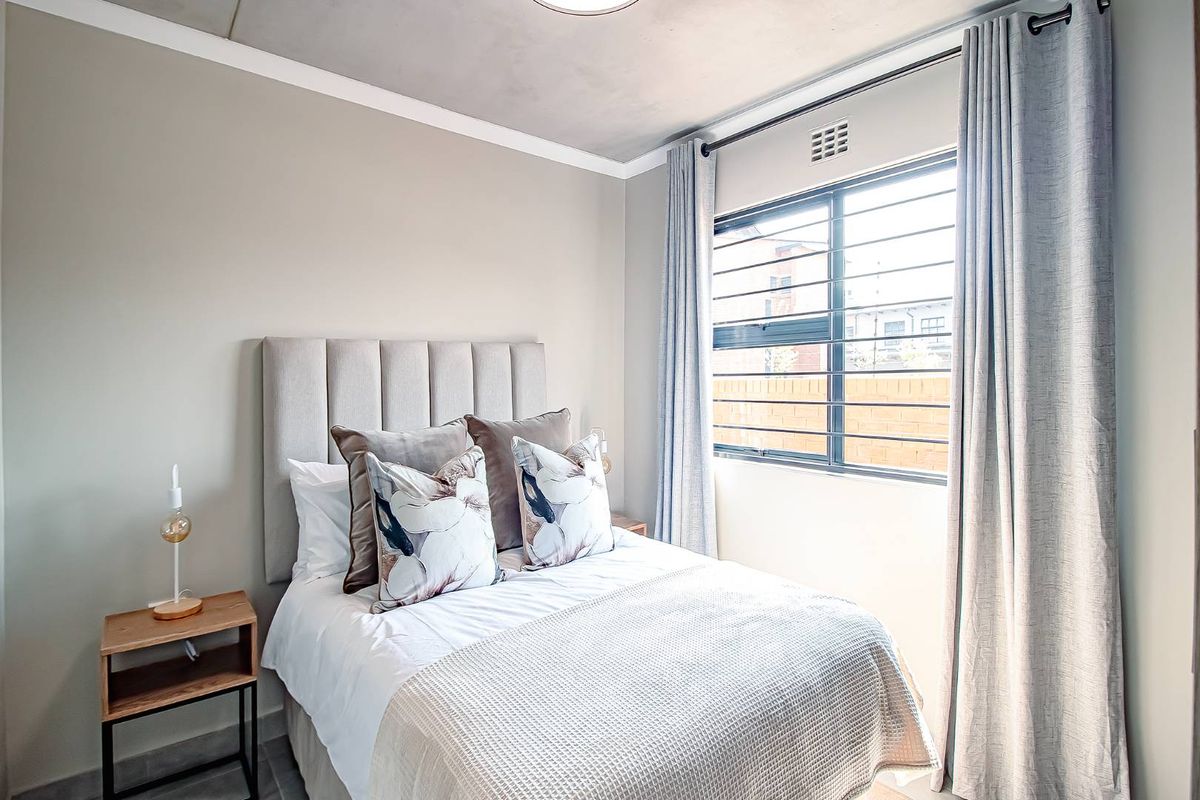 A well-maintained bedroom featuring neutral wall tones, a concrete-look ceiling finish, and a window with integrated security bars.
