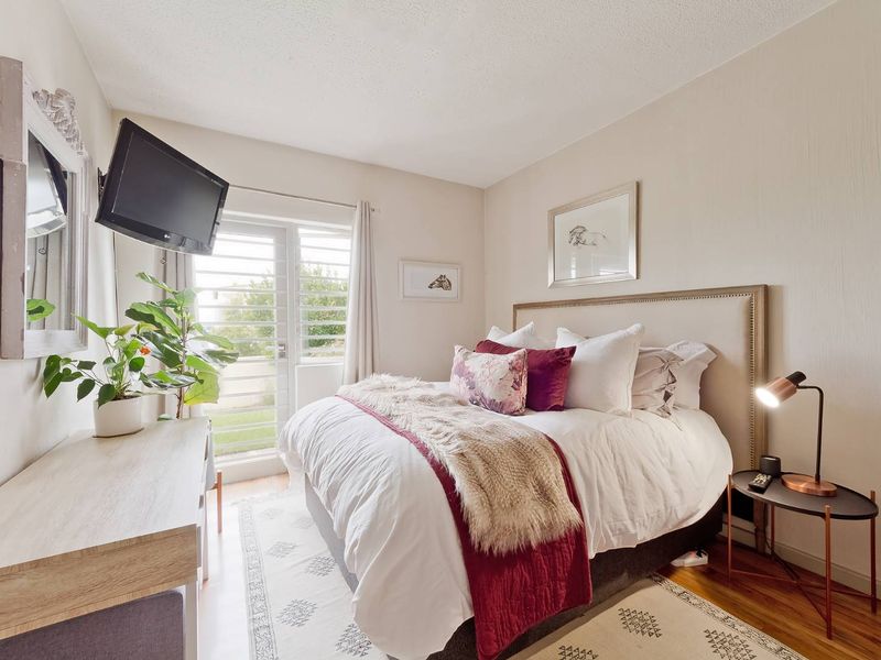 A well-lit bedroom featuring laminate flooring and a glass sliding door with security shutters, providing access to an outdoor area.