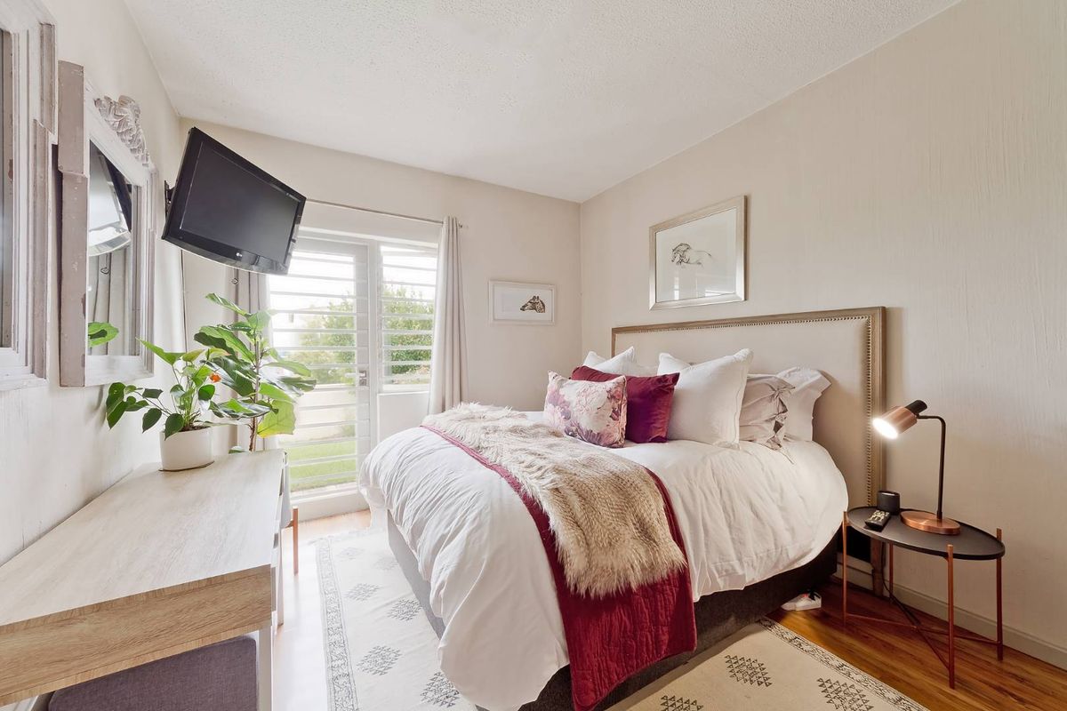 A well-lit bedroom featuring laminate flooring and a glass sliding door with security shutters, providing access to an outdoor area.