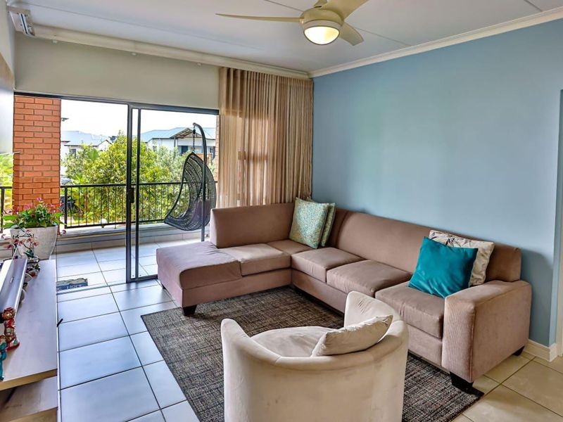 A bright living room featuring tiled flooring, a ceiling fan, and large sliding glass doors that provide direct access to a private balcony.