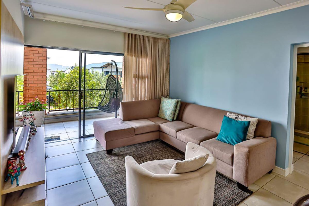 A bright living room featuring tiled flooring, a ceiling fan, and large sliding glass doors that provide direct access to a private balcony.