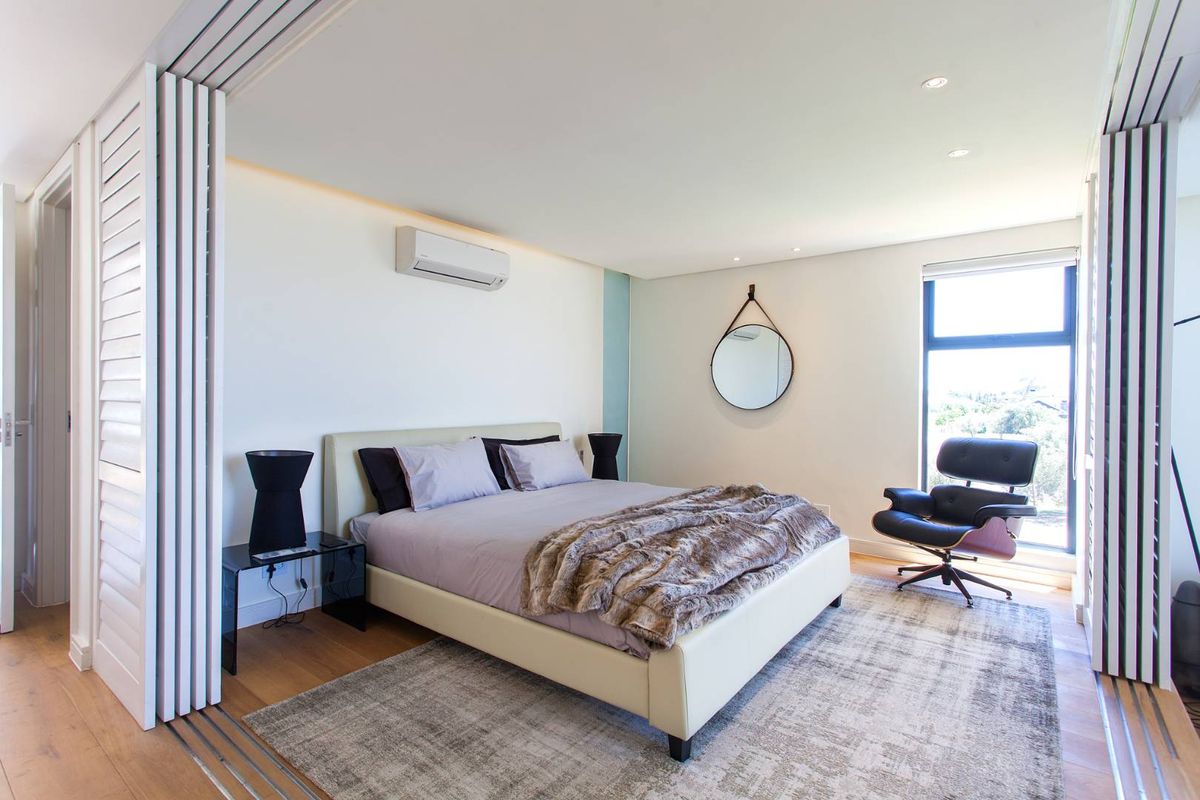 A modern, well-maintained bedroom featuring timber flooring, recessed lighting, an air conditioning unit, and large windows with sliding partition doors.