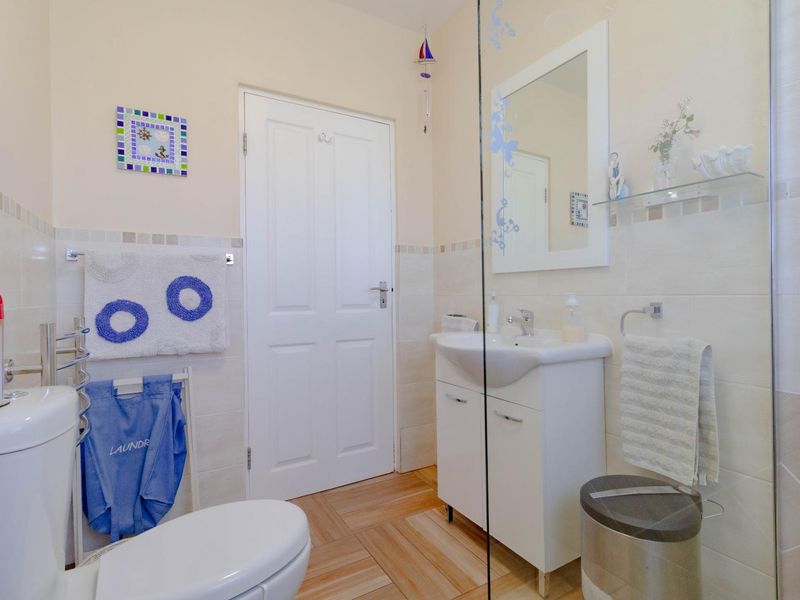 A clean and functional bathroom featuring a vanity cabinet, glass shower screen, and neutral wall tiling.