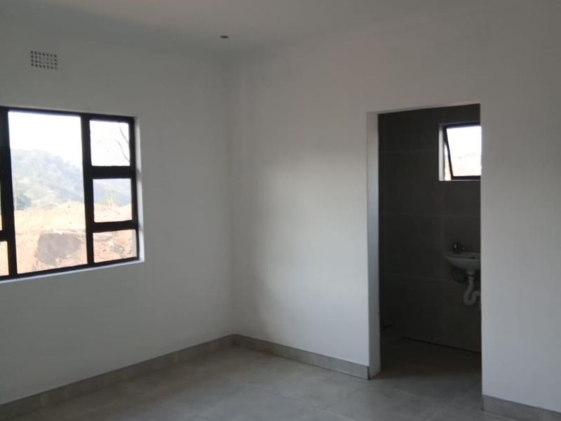 A clean, empty bedroom featuring neutral tiled flooring, modern aluminium window frames, and direct access to an en-suite bathroom.