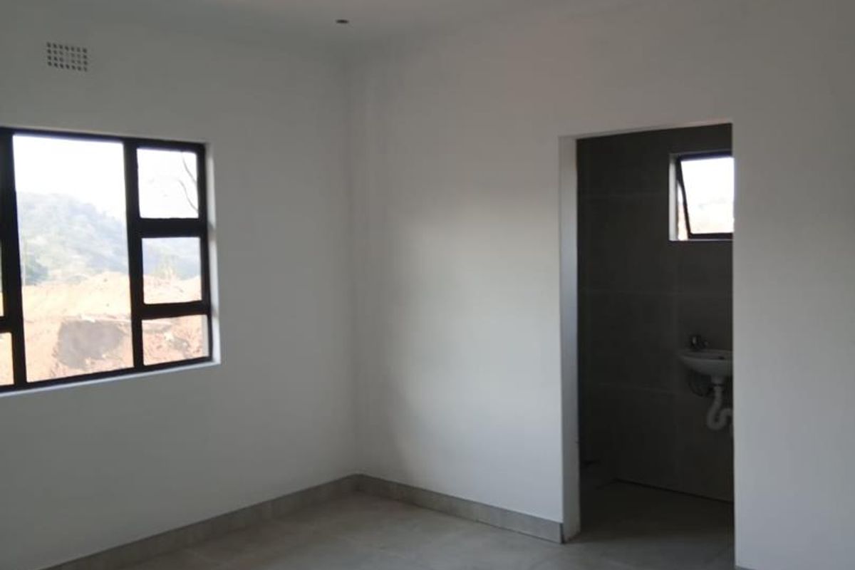 A clean, empty bedroom featuring neutral tiled flooring, modern aluminium window frames, and direct access to an en-suite bathroom.