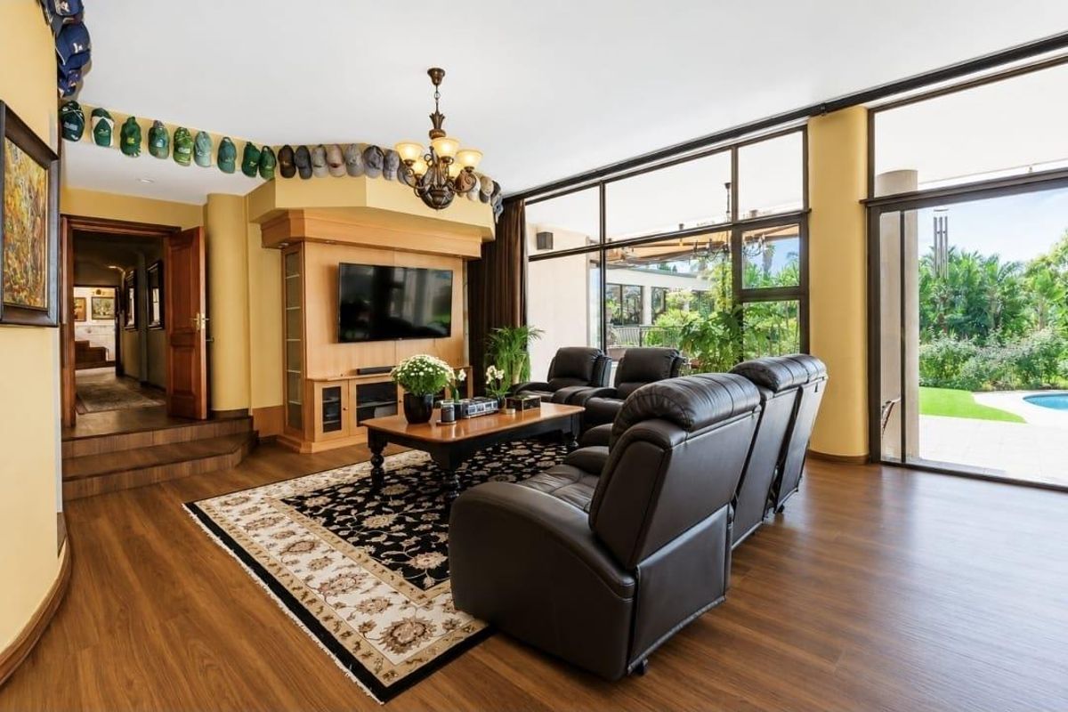Spacious living room featuring large floor-to-ceiling windows, wood-look flooring, and a built-in media cabinet, with direct access to the outdoor patio and pool area.
