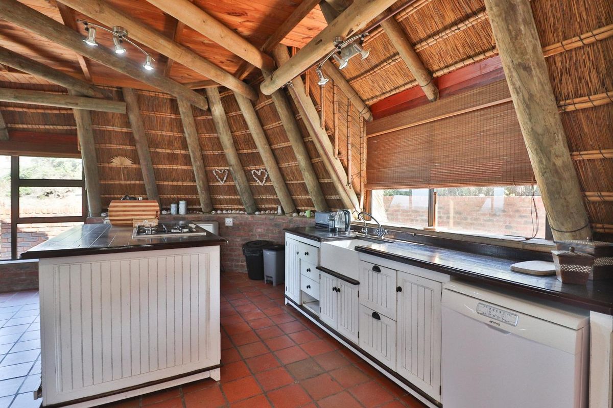 Rustic kitchen featuring a vaulted thatch ceiling with exposed timber beams, farmhouse sink, built-in cabinetry, and a central island with a gas cooktop.