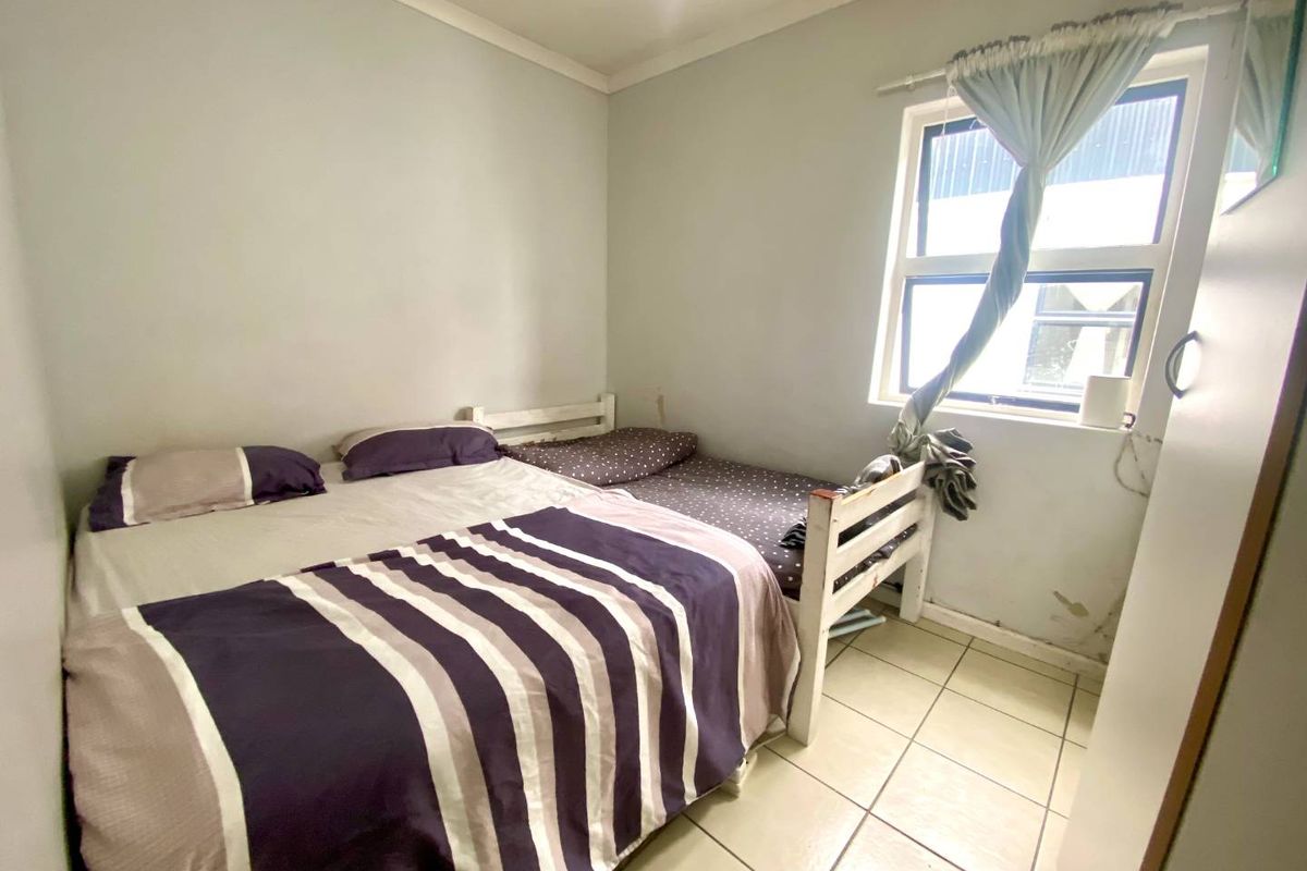A compact bedroom featuring tiled flooring and a window, currently showing signs of wear on the wall finishes near the window frame.