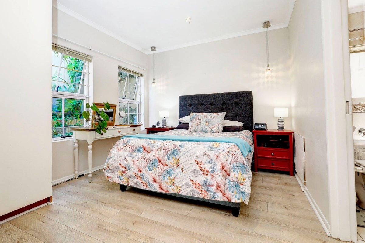 A well-lit bedroom featuring light wood-look flooring, dual windows with garden views, and modern pendant lighting.