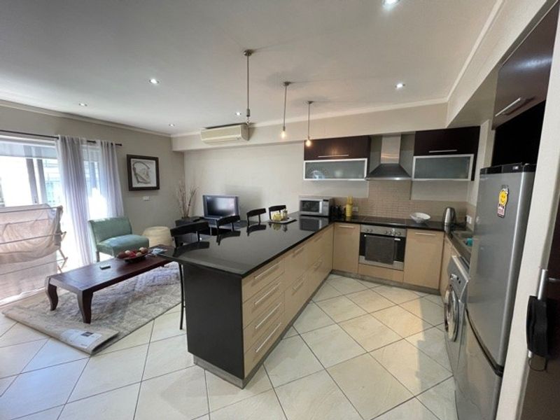Open-plan living area featuring a modern kitchen with granite countertops, built-in appliances, and tiled flooring, seamlessly flowing into the adjacent living space.