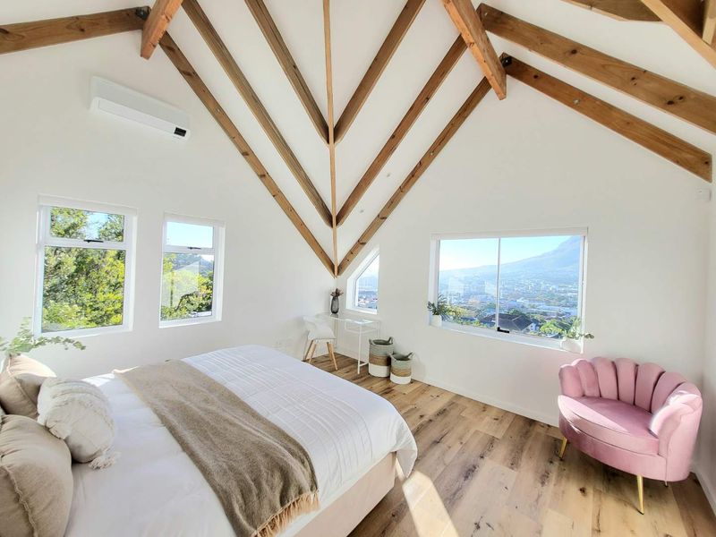 Spacious bedroom featuring vaulted ceilings with exposed timber trusses, laminate flooring, split-system air conditioning, and large windows offering scenic mountain and city views.