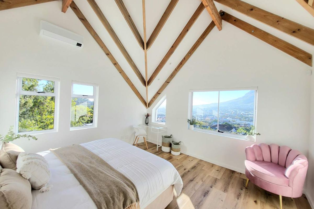 Spacious bedroom featuring vaulted ceilings with exposed timber trusses, laminate flooring, split-system air conditioning, and large windows offering scenic mountain and city views.