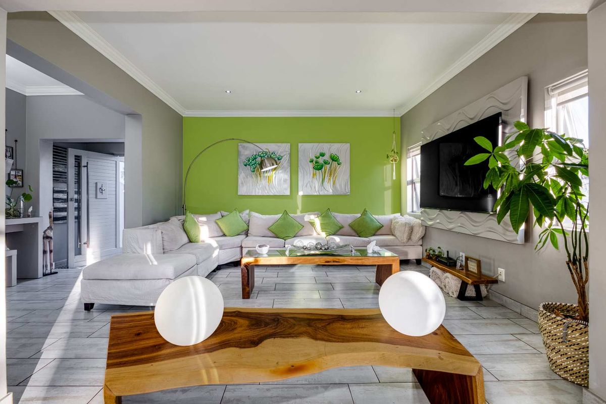 A bright and spacious living room featuring tiled flooring, recessed ceiling lighting, and a decorative feature wall.