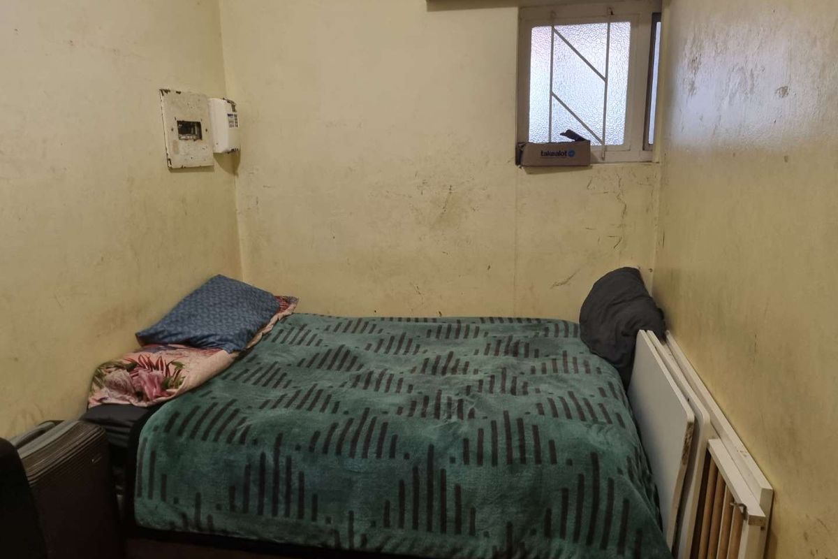 A compact bedroom featuring a small window with security bars and an electrical distribution board mounted on the wall.