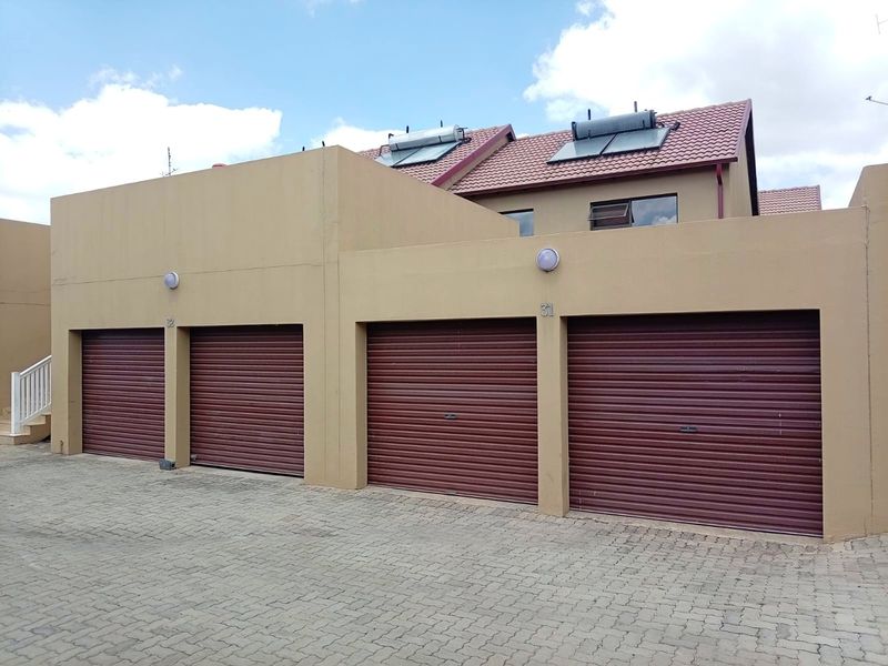 Exterior view of a townhouse complex featuring multiple roller shutter garage doors, paved driveway access, and roof-mounted solar water heating systems.