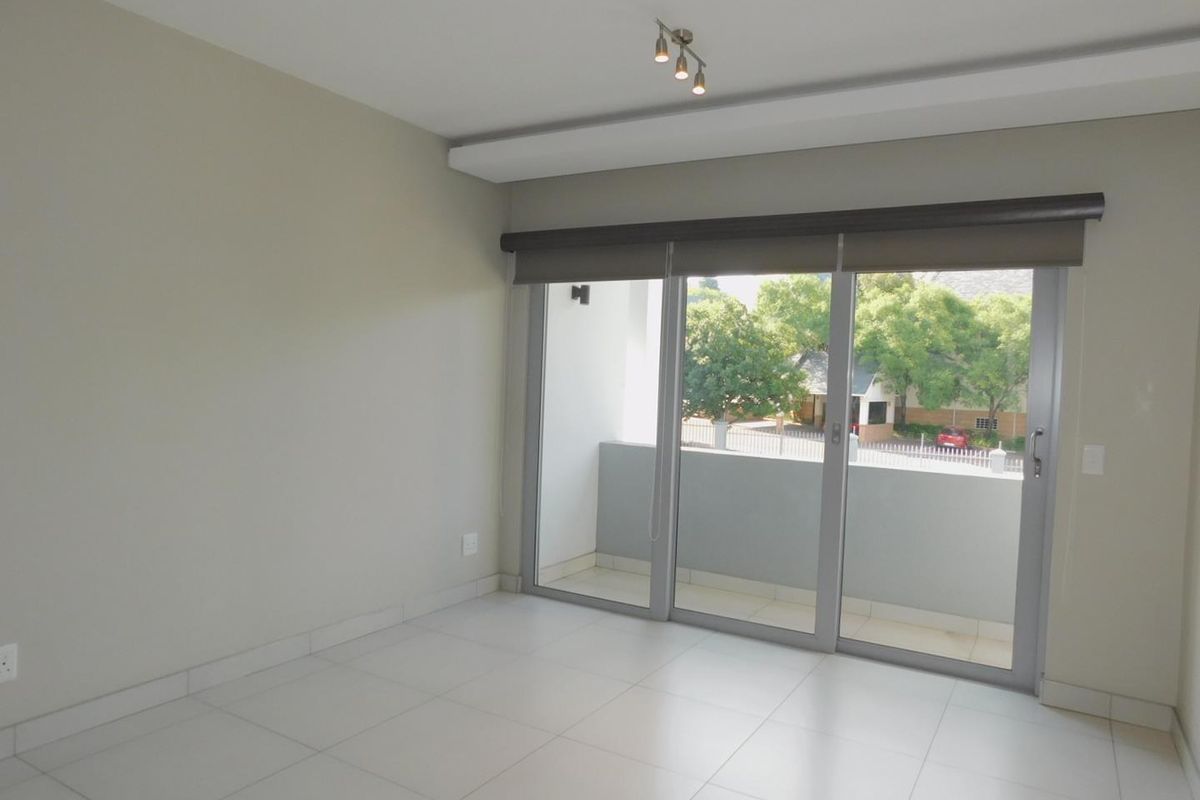 A bright, empty living area featuring neutral tiled floors, modern recessed ceiling lighting, and large sliding glass doors opening onto a private balcony.