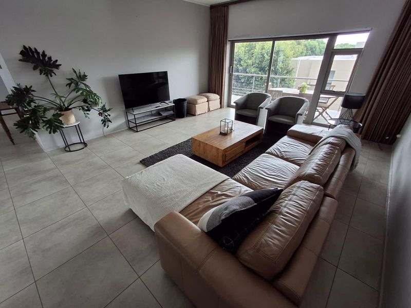 Spacious living room featuring large format floor tiles and a wide sliding glass door providing access to an outdoor balcony area.