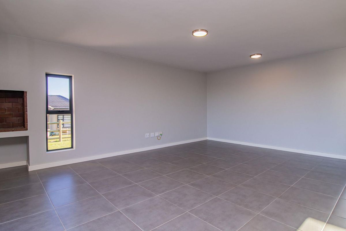 A spacious, empty living room featuring neutral grey tiled flooring, recessed ceiling lighting, and a built-in brick fireplace.