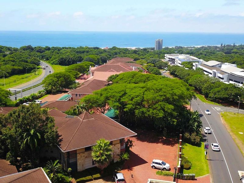 Aerial view of the office property complex, showcasing the building architecture, surrounding landscaped grounds, paved access roads, and proximity to the coastline.