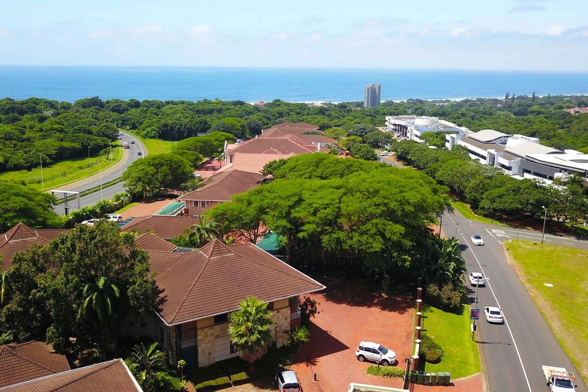 Aerial view of the office property complex, showcasing the building architecture, surrounding landscaped grounds, paved access roads, and proximity to the coastline.