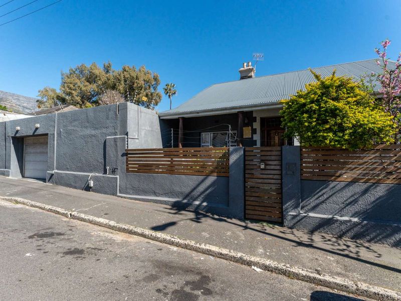 Front elevation of a house featuring a corrugated metal roof, timber slat fencing, and a secure rendered boundary wall with an integrated garage.