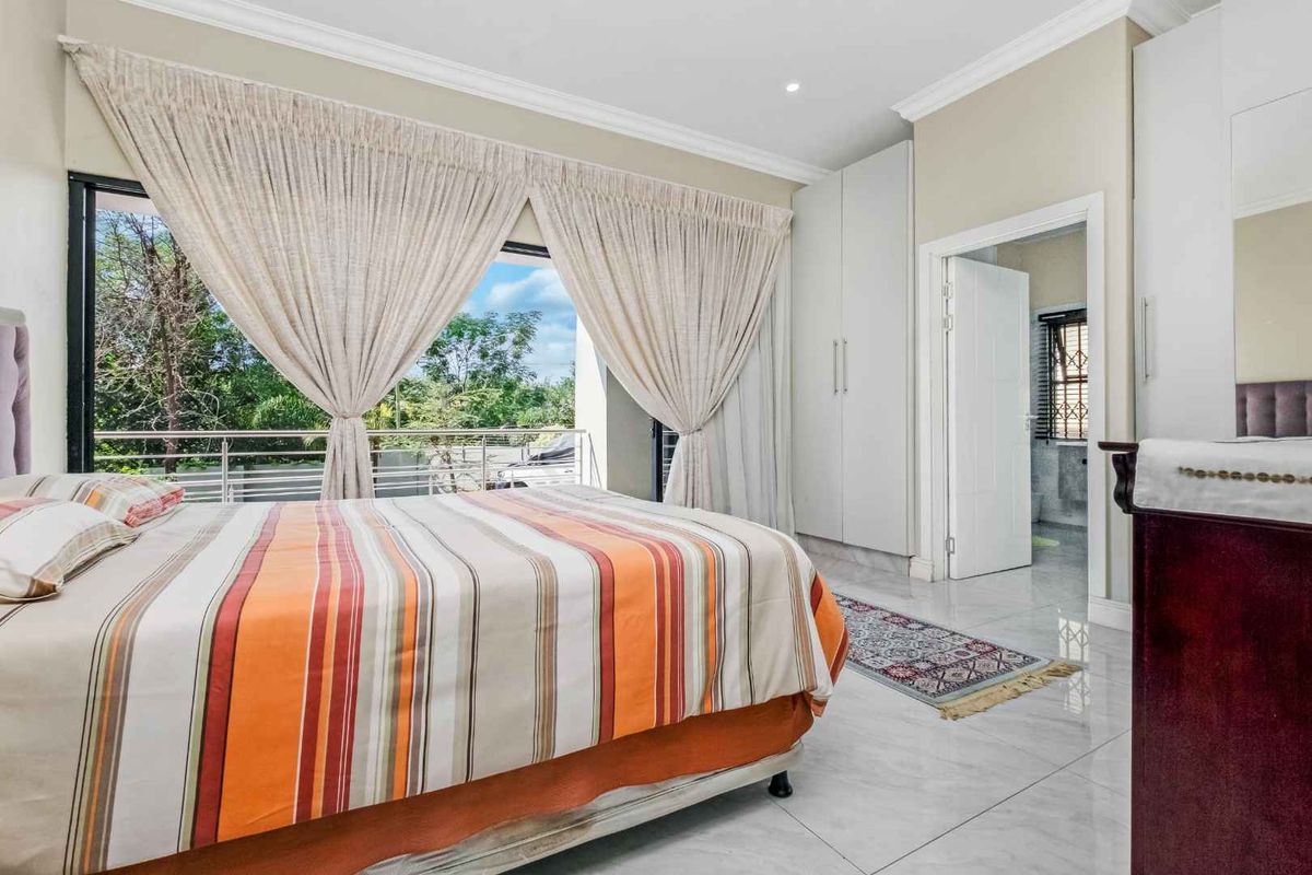 Spacious bedroom featuring large windows with balcony access, built-in cupboards, and polished tile flooring, leading into an adjoining bathroom.
