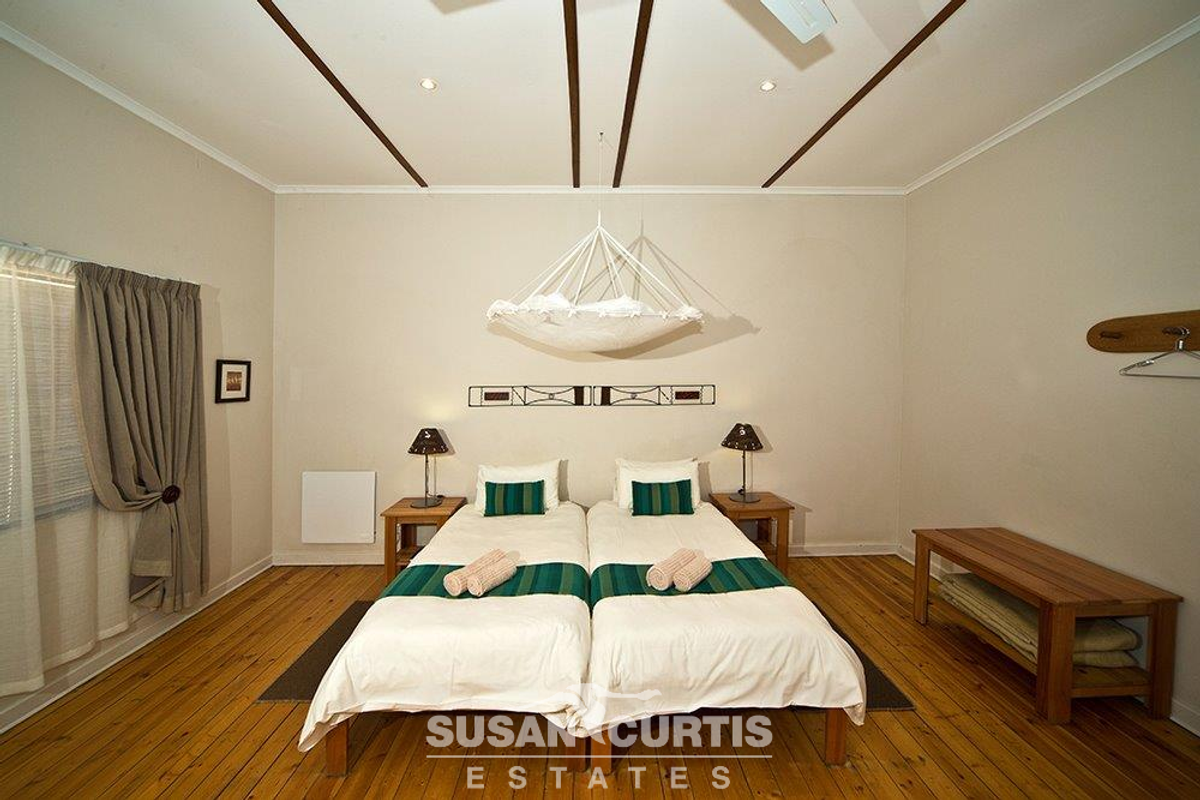 A well-maintained hotel bedroom featuring polished wooden flooring, recessed ceiling lighting, and decorative ceiling beams.