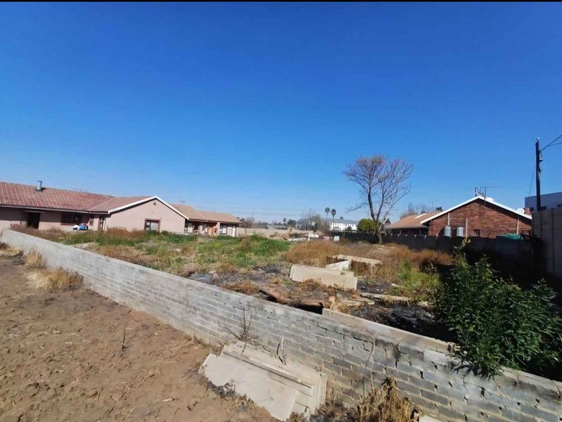 A view of a vacant, unmaintained rear plot featuring a perimeter brick boundary wall and surrounding residential properties.