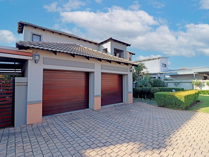 A well-maintained front exterior view featuring a double garage with wooden doors, a paved driveway, and a neatly landscaped garden.