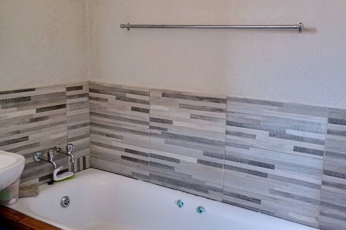 A functional bathroom featuring a bathtub with decorative tiled splashback, a pedestal basin, and a wall-mounted towel rail.