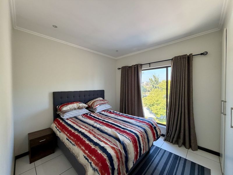 A well-maintained bedroom featuring tiled flooring, recessed downlighting, and a built-in wardrobe with a large window providing natural light and exterior views.