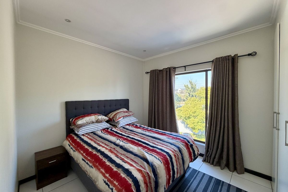 A well-maintained bedroom featuring tiled flooring, recessed downlighting, and a built-in wardrobe with a large window providing natural light and exterior views.