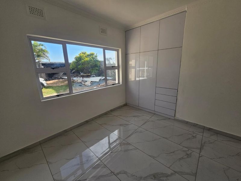 A bright, empty bedroom featuring modern white built-in cupboards, large windows, and polished marble-look floor tiles.